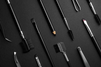 Set of professional eyebrow tools on black background, flat lay