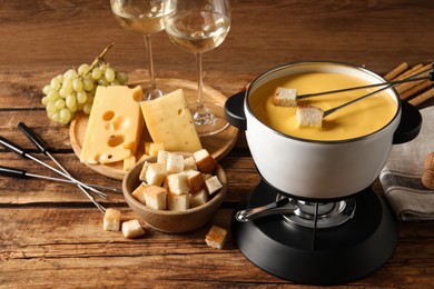 Photo of Pot of tasty cheese fondue, snacks and wine on wooden table
