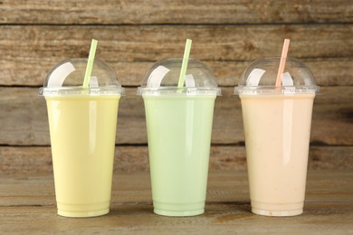 Photo of Plastic cups with different tasty smoothies on wooden table