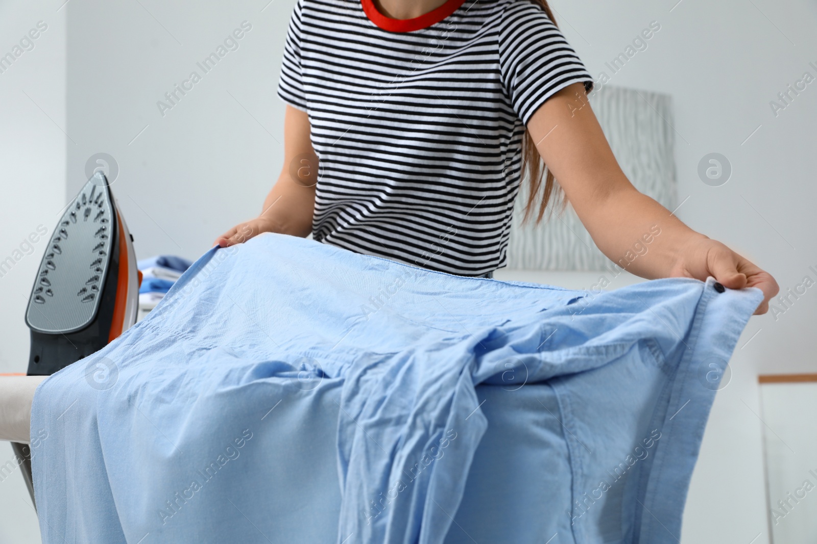 Photo of Young woman ironing clothes on board at home, closeup