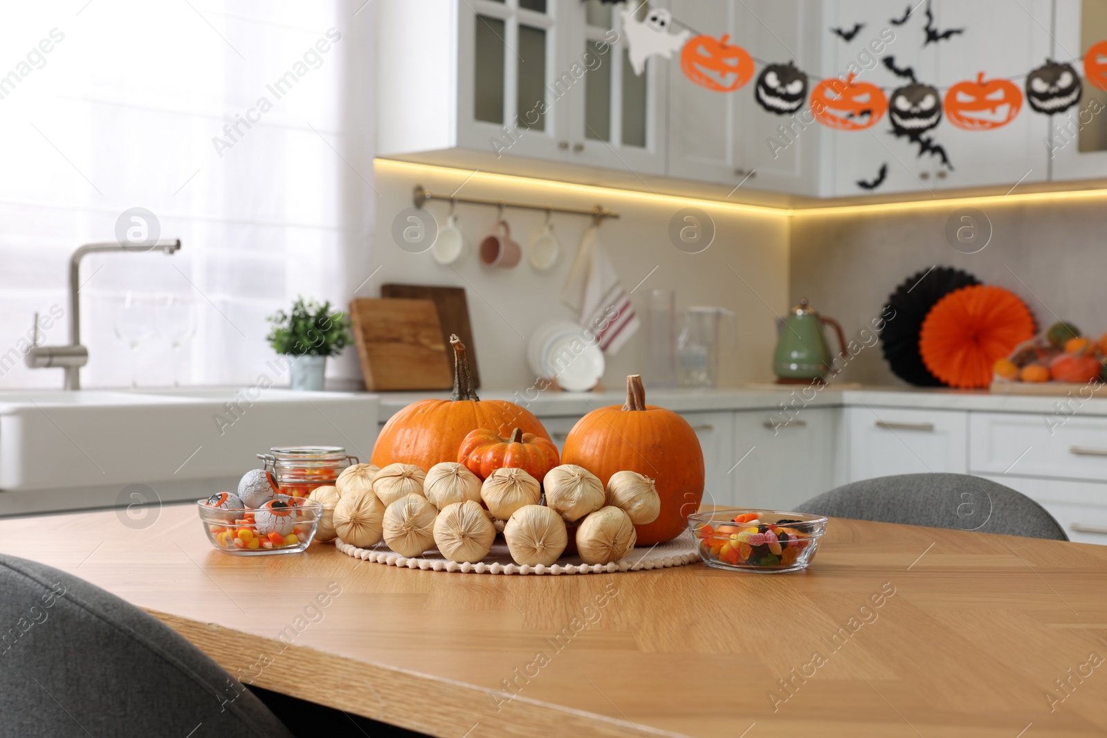 Photo of Kitchen decorated for Halloween. Pumpkins, jelly candies and bunch of garlic on wooden table