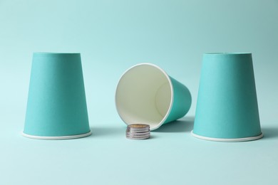 Three paper cups and coins on light blue background. Thimblerig game