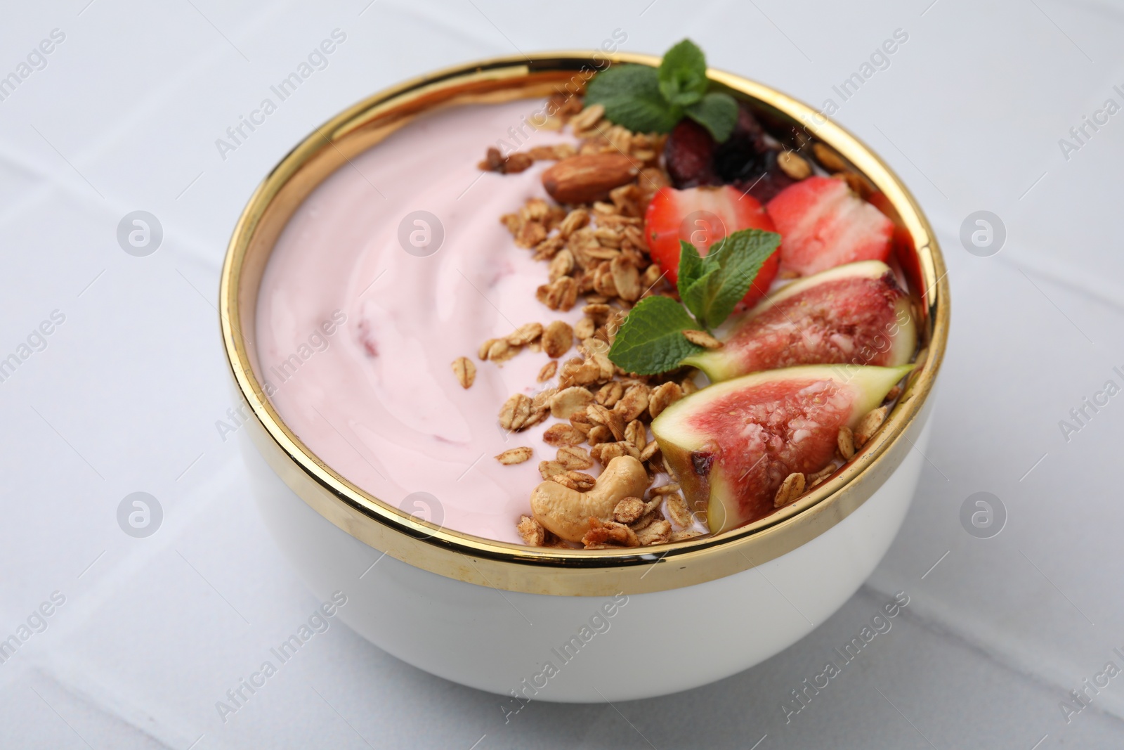 Photo of Bowl with yogurt, fruits and granola on white tiled table, closeup