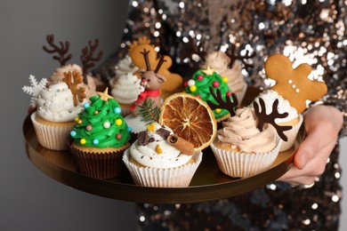 Photo of Woman holding tasty Christmas cupcakes on light background, closeup