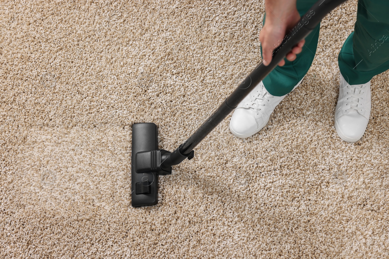 Photo of Dry cleaner's employee hoovering carpet with vacuum cleaner, above view