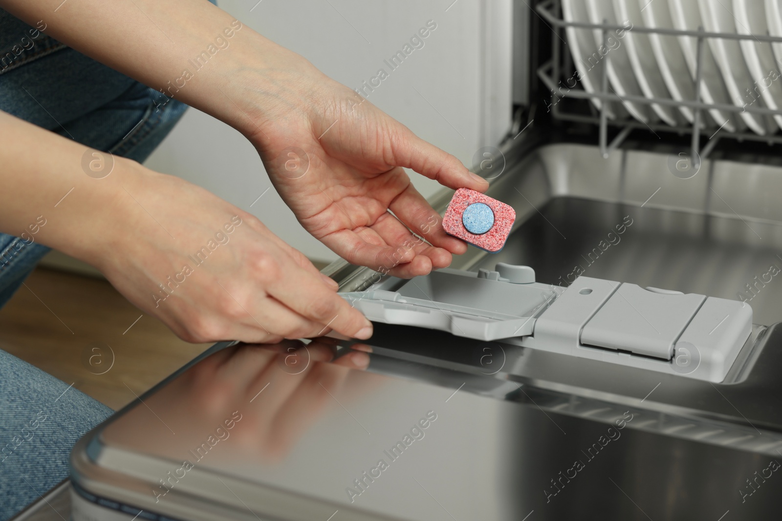 Photo of Woman putting detergent tablet into open dishwasher, closeup