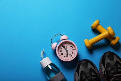 Photo of Sneakers, dumbbells and alarm clock on light blue background, flat lay with space for text. Morning exercise
