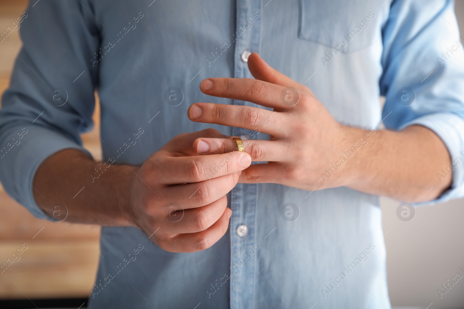 Photo of Man taking off wedding ring on blurred background, closeup. Divorce concept