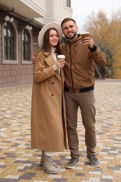 Photo of Happy couple wearing stylish autumn clothes with cups of coffee on city street