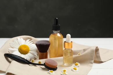 Photo of Essential oil, chamomiles and brushes on table against dark background