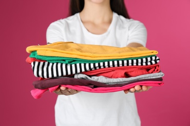 Photo of Young woman holding clean laundry on color background, closeup