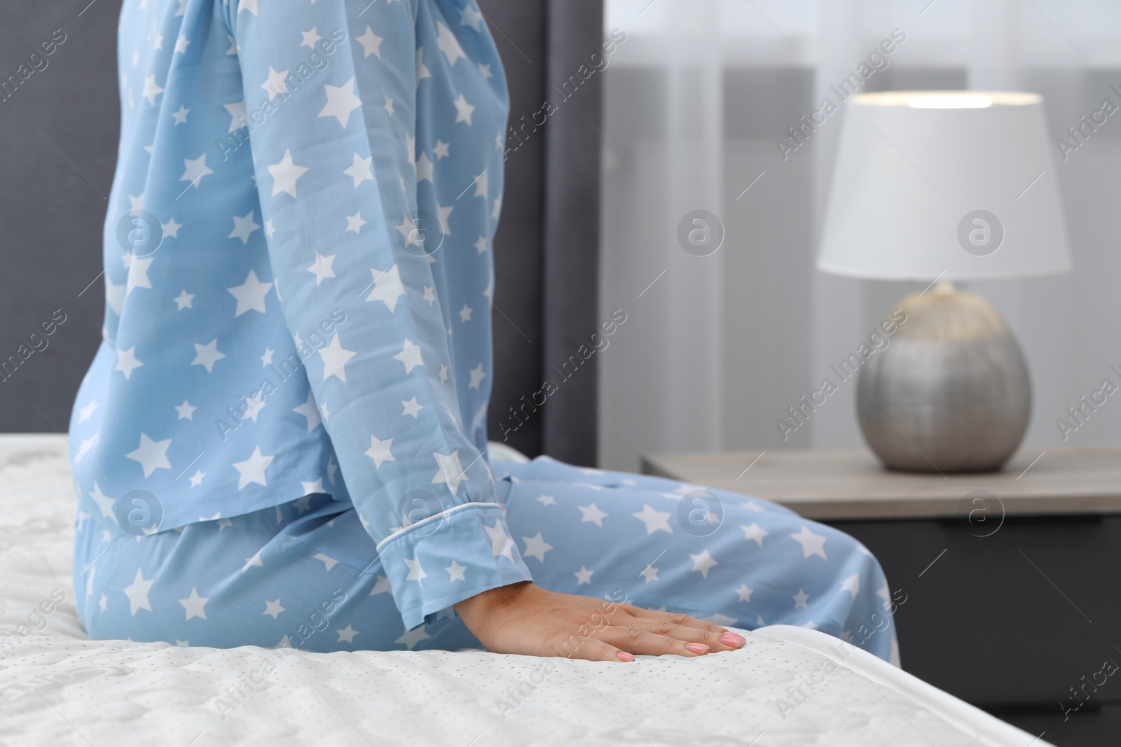 Photo of Woman sitting on new soft mattress in bedroom, closeup