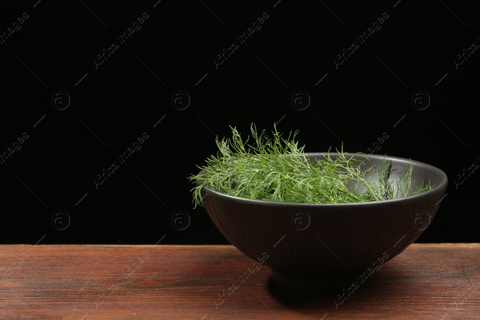 Photo of Bowl of fresh green dill on wooden table against black background. Space for text