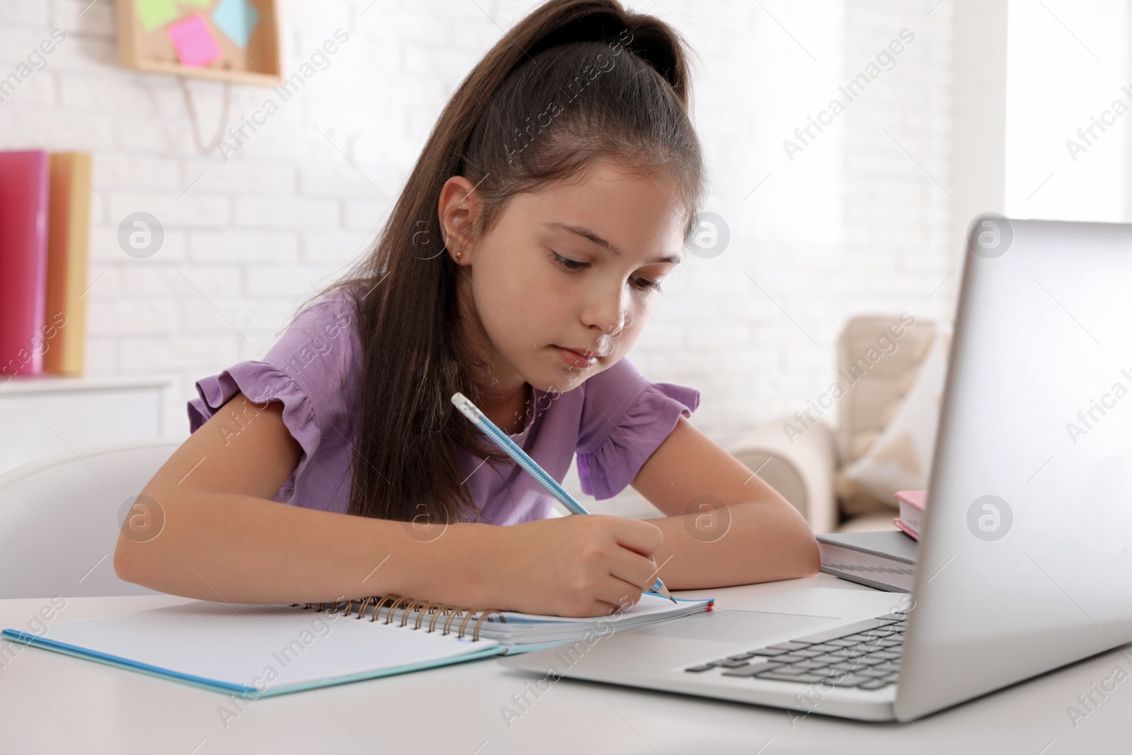 Photo of Pretty preteen girl doing homework with laptop at table