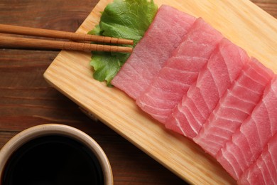 Photo of Tasty sashimi (pieces of fresh raw tuna), lettuce, soy sauce and chopsticks on wooden board, flat lay