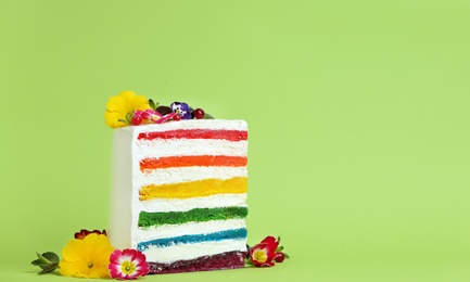 Photo of Slice of delicious rainbow cake with flowers on color background