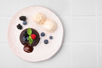 Plate with delicious chocolate fondant, berries, ice cream and mint on white tiled table, top view. Space for text