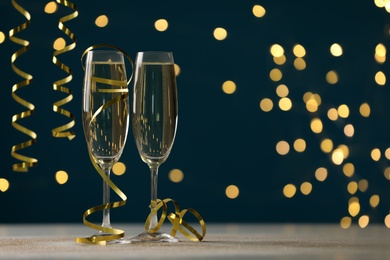 Photo of Glasses of champagne and serpentine streamers on table against dark blue background with blurred lights. Space for text