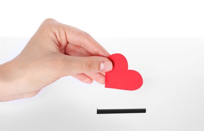 Photo of Woman putting red heart into slot of donation box against white background, closeup