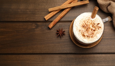 Photo of Cup of hot drink with whipped cream and aromatic cinnamon on wooden table, flat lay. Space for text