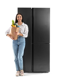 Photo of Young woman with bag of groceries near refrigerator on white background