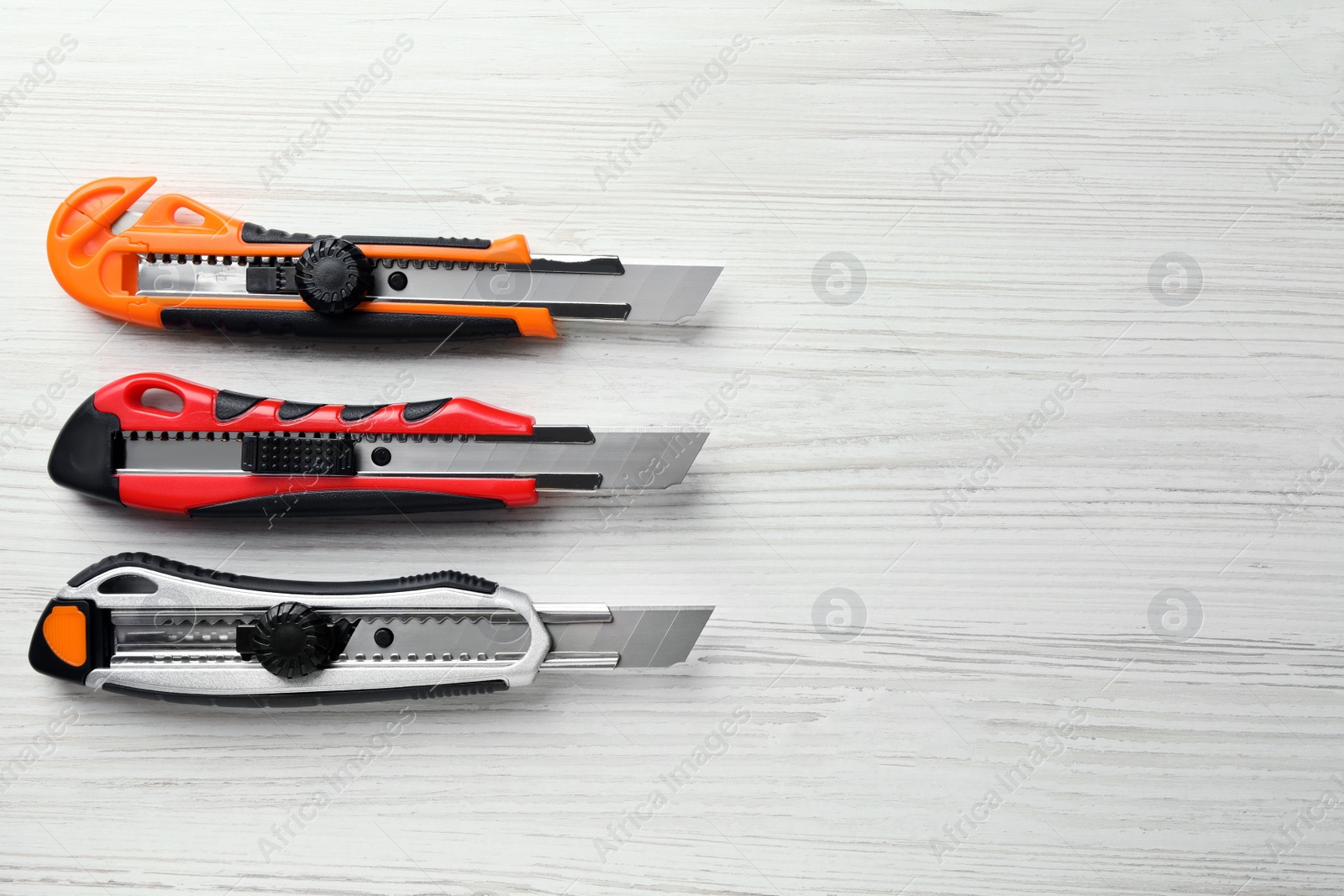 Photo of Different utility knives on white wooden table, flat lay. Space for text
