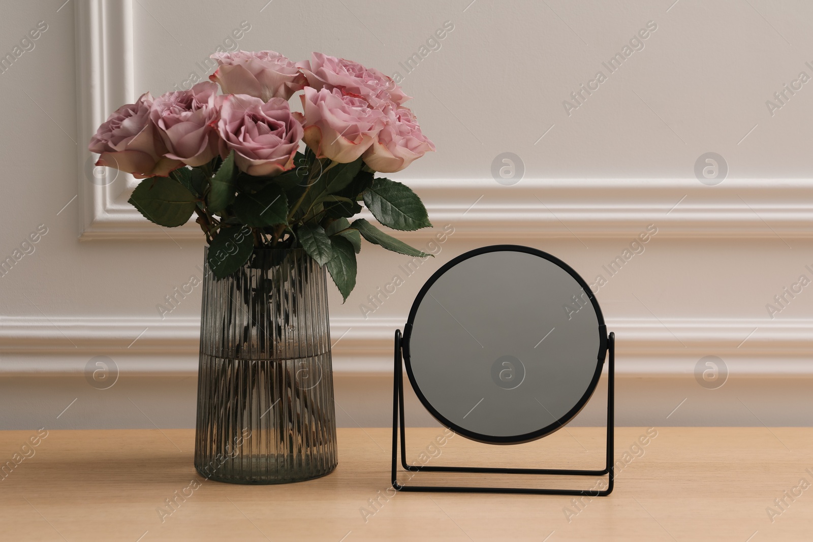 Photo of Mirror and vase with pink roses on wooden dressing table