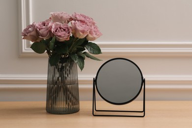 Photo of Mirror and vase with pink roses on wooden dressing table