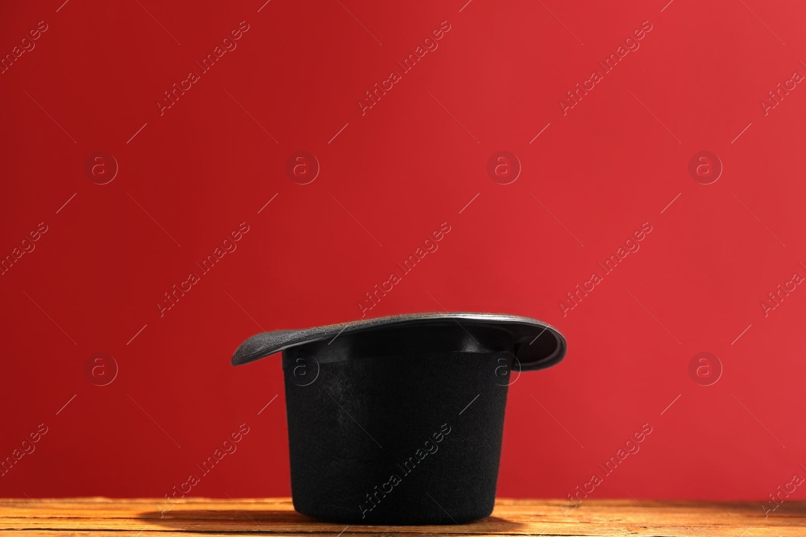 Photo of Magician's hat on wooden table against red background