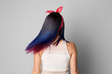 Photo of Young woman with bright dyed hair on grey background, back view