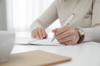 Photo of Left-handed woman writing in notebook at table indoors, closeup. Space for text