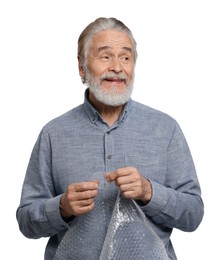 Happy senior man popping bubble wrap on white background. Stress relief