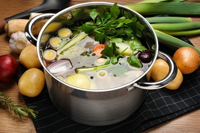 Photo of Pot and different ingredients for cooking tasty bouillon on wooden table