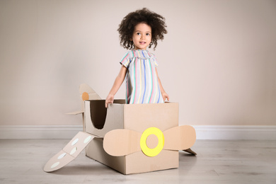 Photo of Cute African American child playing with cardboard plane near beige wall