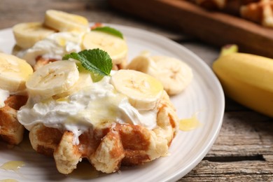 Photo of Delicious Belgian waffles with banana and whipped cream on wooden table, closeup