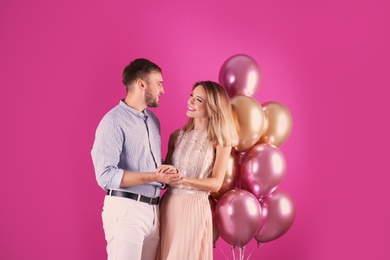 Young couple with air balloons on color background