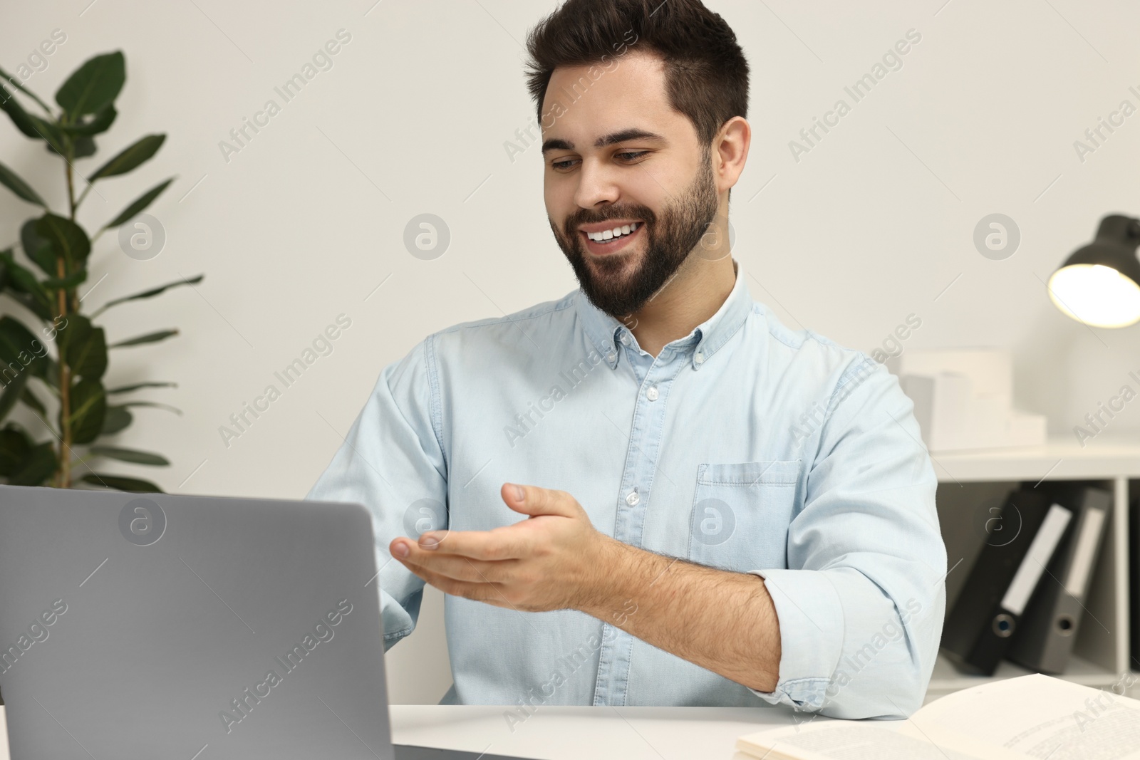 Photo of Young man having video chat via laptop at table indoors