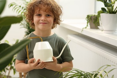 Photo of Cute little boy holding watering can near beautiful green plants at home. House decor