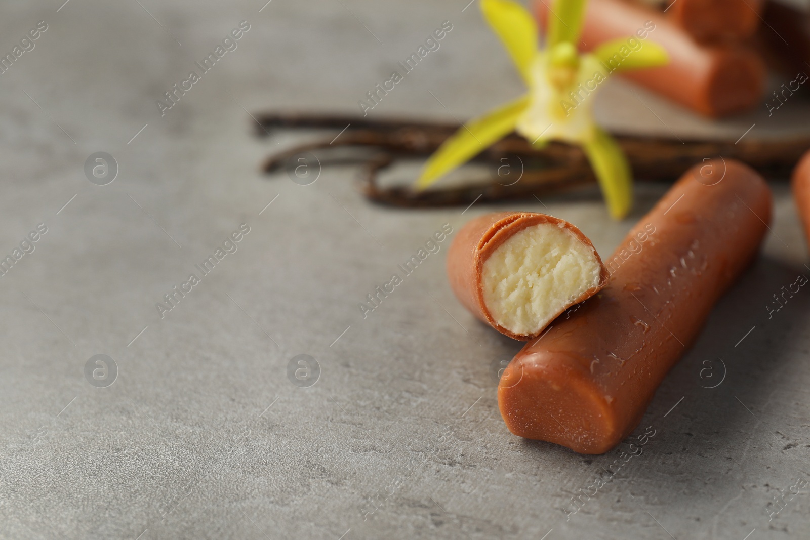 Photo of Glazed curd cheese bars, vanilla pods and flower on grey table, closeup. Space for text