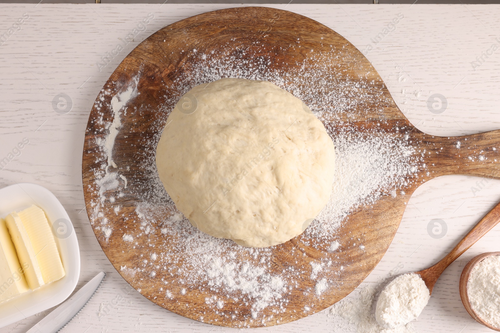 Photo of Fresh dough sprinkled with flour and other ingredients on white wooden table, flat lay