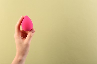 Woman with pink makeup sponge on light yellow background, closeup. Space for text