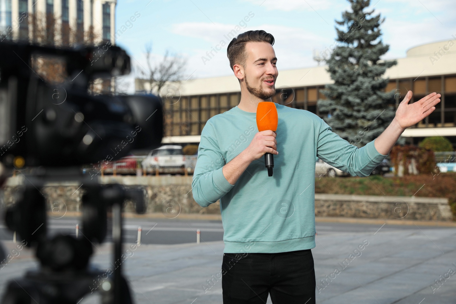 Photo of Young male journalist with microphone working on city street