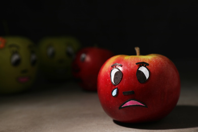 Photo of Apple with crying face on grey table, closeup. Concept of jealousy
