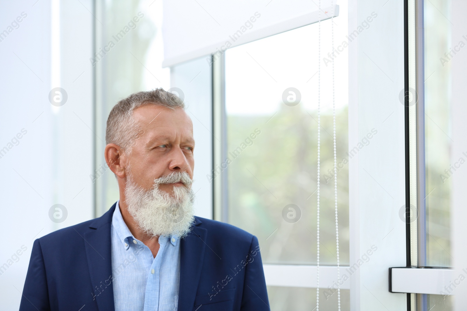 Photo of Portrait of handsome mature man in elegant suit looking out window indoors