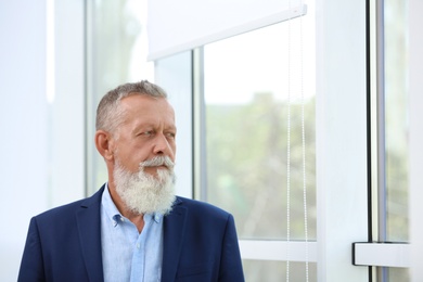 Portrait of handsome mature man in elegant suit looking out window indoors