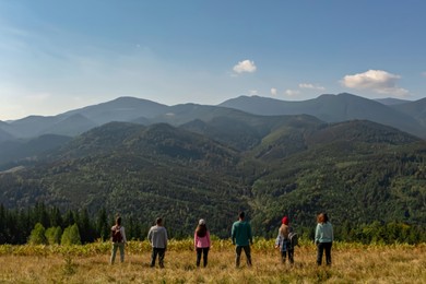 Group of tourists on hill in mountains, back view