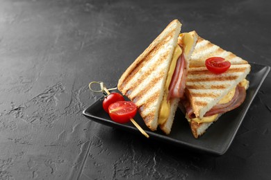 Photo of Tasty sandwiches with ham, melted cheese and tomatoes on black textured table, space for text