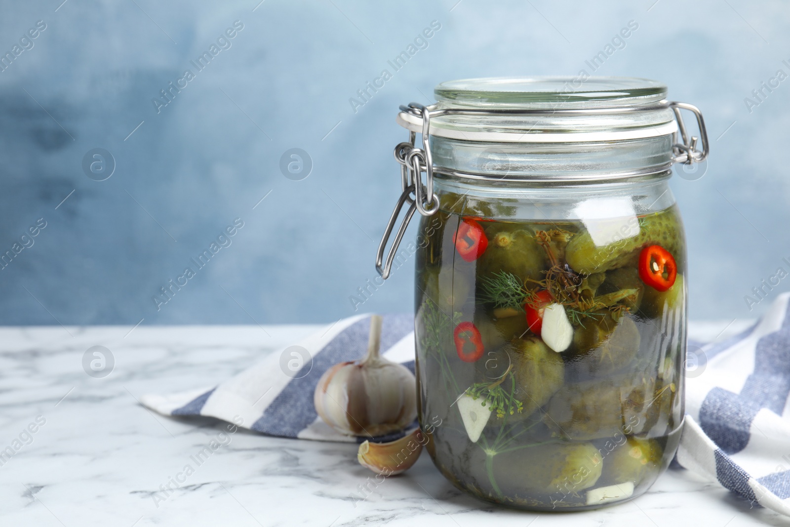Photo of Jar with pickled cucumbers on marble table against blue background, space for text