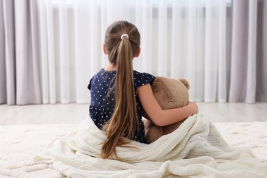 Photo of Cute little girl with teddy bear at home, back view
