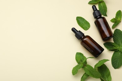 Photo of Bottles of essential oil and mint on beige background, flat lay. Space for text